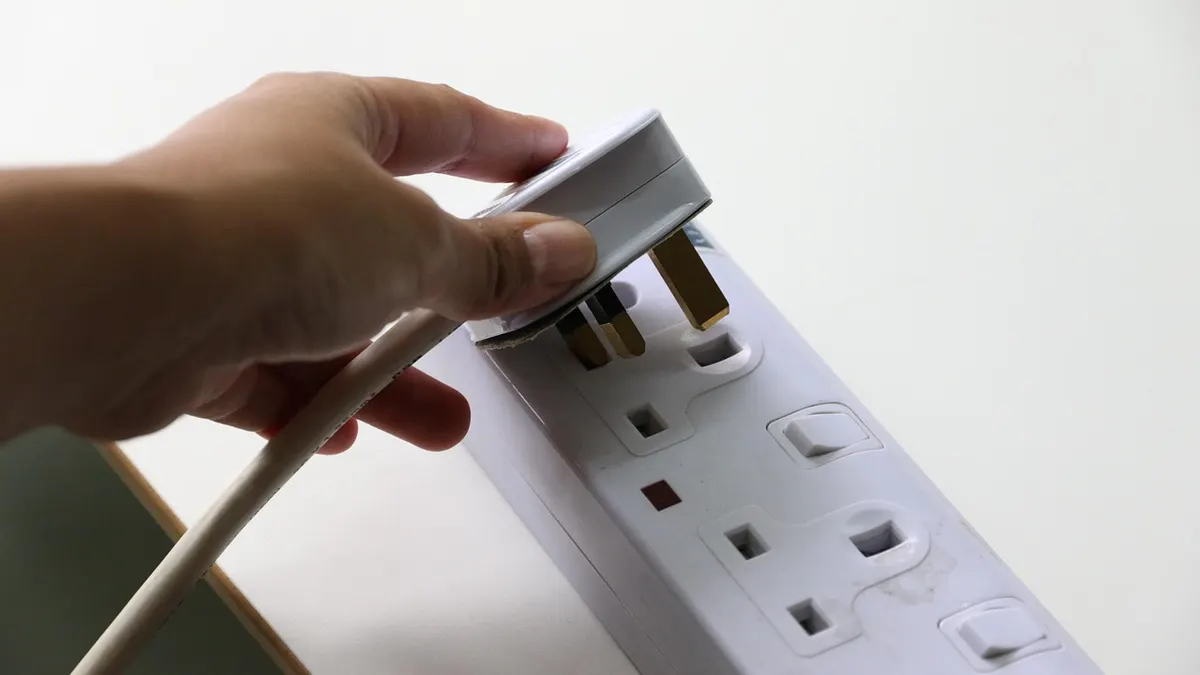 Mão encaixando plugue em régua de tomadas
