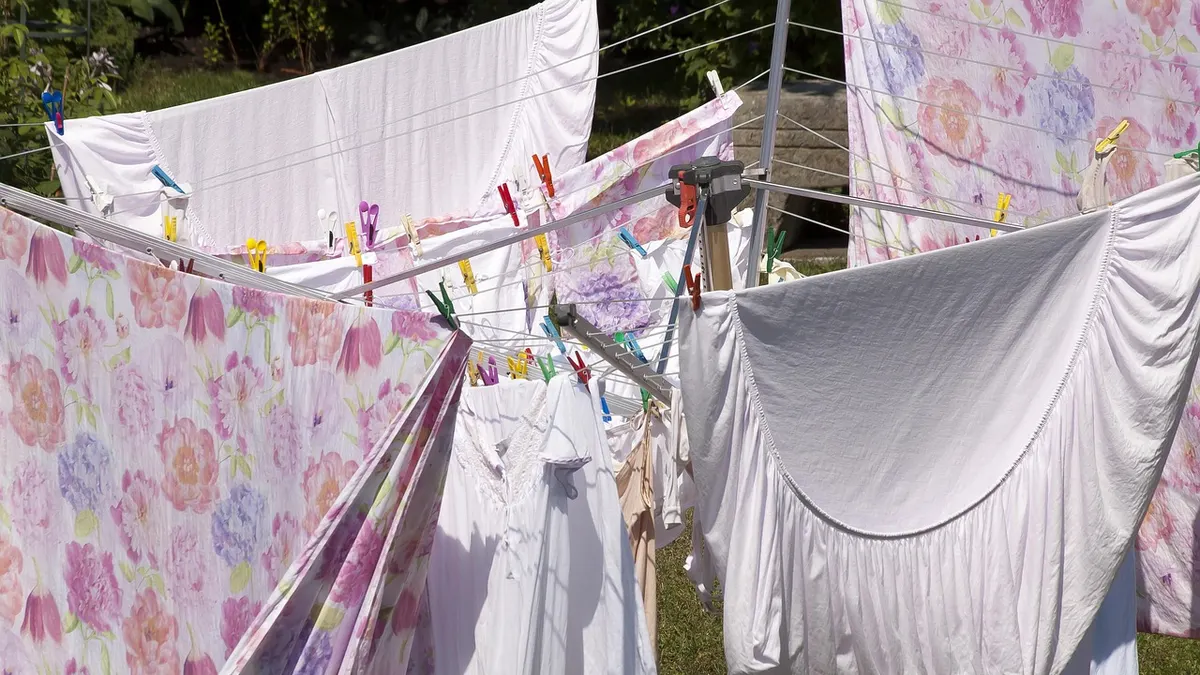 Lençóis e roupas claras secando em varal giratório no jardim